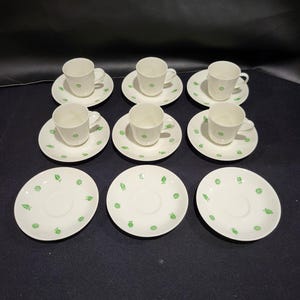 May include: A set of six white teacups and saucers with a green floral design. The cups and saucers are arranged in two rows of three.