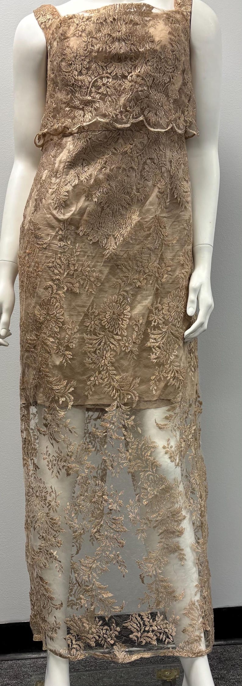 Pode incluir: Um vestido comprido sem mangas com uma sobreposi&ccedil;&atilde;o transparente. O vestido &eacute; feito de um delicado tecido de renda floral em uma cor marrom claro.