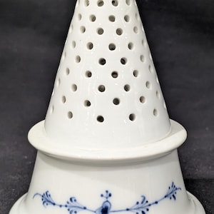 May include: White ceramic kitchen utensil with a conical, perforated top and a flared base. The base features a blue floral design. The utensil is likely a salt shaker or a similar kitchen tool.