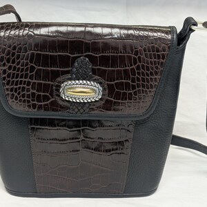May include: A black and brown crossbody bag with a textured, faux crocodile pattern. The bag features a flap closure with a decorative silver and gold accent. The adjustable strap is black, and the bag has a structured shape.