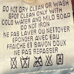 May include: A close-up of a white fabric tag with black text. The tag provides care instructions: "DO NOT DRY CLEAN OR WASH", "SPOT CLEAN ONLY", "DO NOT IRON", and other washing instructions. There are also several laundry symbols.