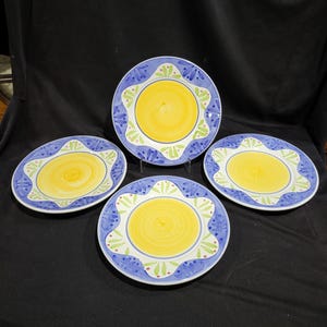 May include: Set of four ceramic dinner plates with a blue and yellow floral design. The plates have a yellow center with a blue rim and a floral pattern in blue, green, and yellow.