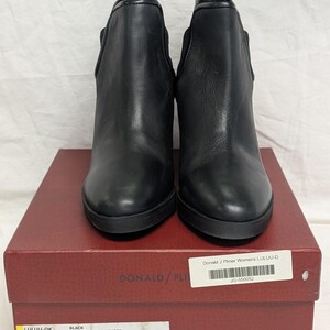 May include: A pair of black leather ankle boots with a rounded toe and a stacked heel. The boots are displayed on a red box with the brand name "DONALD/PLINER" visible. The box also has product information including the style name "LULUU-DK".