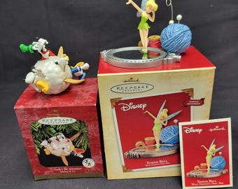 May include: A collection of Disney Hallmark Keepsake ornaments. The ornaments include Tinker Bell, a blue yarn ball, and a figurine of Goofy's Ski Adventure. The boxes are red and gold.