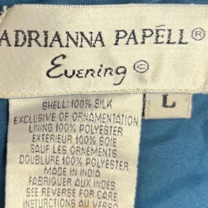 May include: Close-up of a label from an Adrianna Papell Evening garment. The label is cream-colored with black text, including the brand name, "Evening," and fabric composition details. The size is indicated as "L."