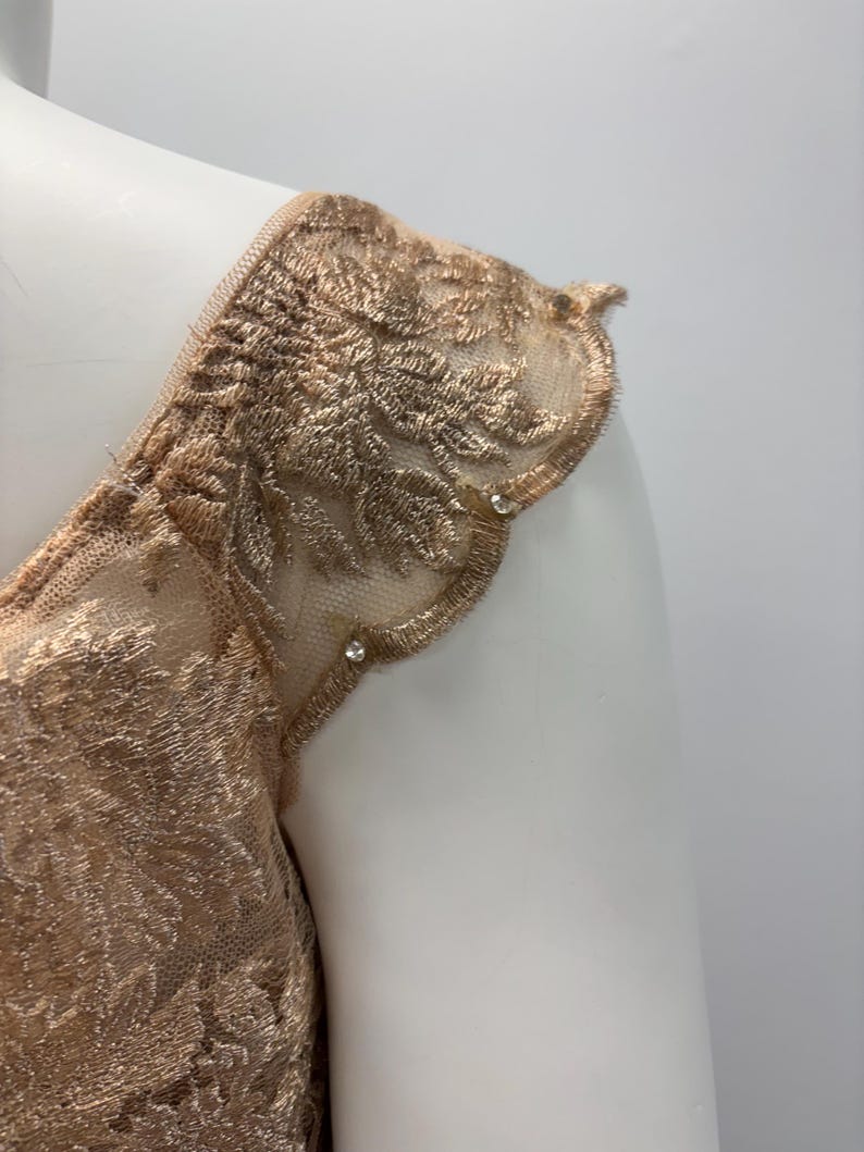 Pode incluir: Close-up de um tecido de renda dourado com uma borda festoneada e pequenas p&eacute;rolas. O tecido &eacute; transparente e delicado, com um padr&atilde;o floral.