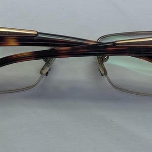 May include: Versace eyeglasses with a tortoiseshell pattern on the frames and temples. The frames have a gold accent and the brand name is visible on the temples. The lenses are clear.