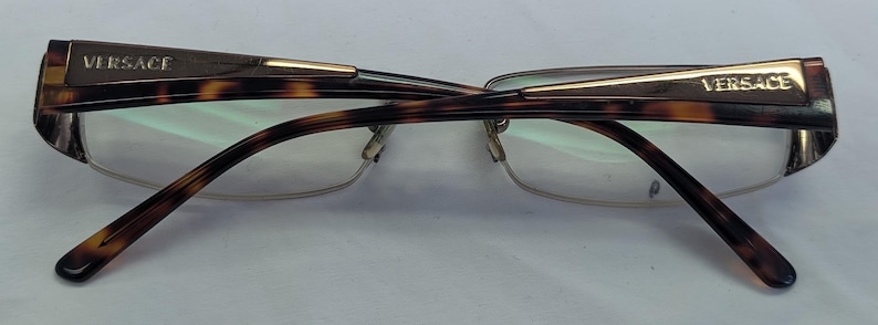 May include: Versace eyeglasses with a tortoiseshell pattern on the frames and temples. The frames have a gold accent and the brand name is visible on the temples. The lenses are clear.