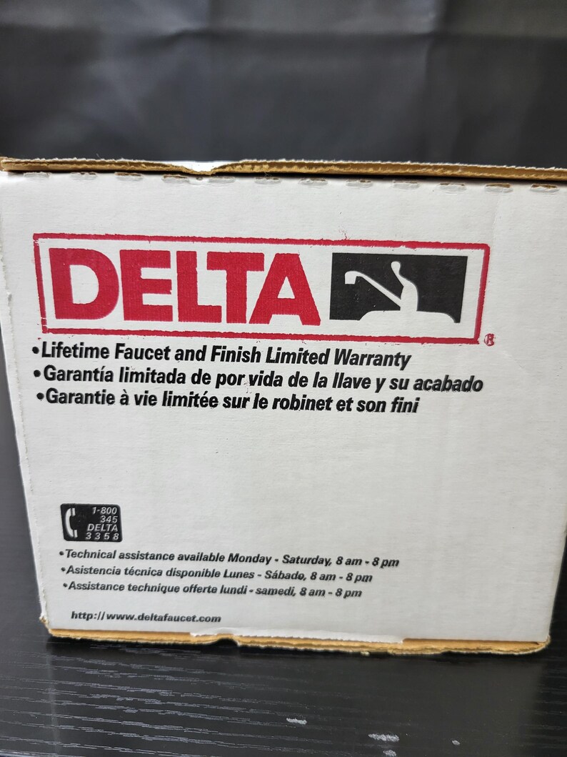 May include: A white box with the Delta logo and the text "Lifetime Faucet and Finish Limited Warranty". The box also includes the text "Garant&iacute;a limitada de por vida de la llave y su acabado" and "Garantie &agrave; vie limit&eacute;e sur le robinet et son fini". The box also includes a phone number and website address.