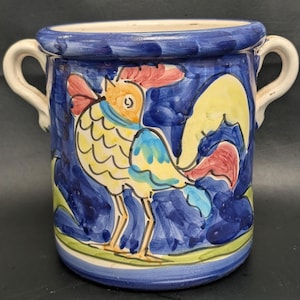 May include: A hand-painted ceramic jar with a rooster design. The jar is blue with a white rim and handles. The rooster is yellow, red, and blue. The jar is approximately 5 inches tall and 4 inches in diameter.