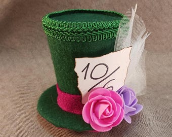 May include: A green felt hat with a red band and a white tag that says "10%". The hat has a white tulle bow and is decorated with pink and purple flowers.