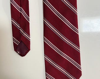 May include: A burgundy tie with a diagonal striped pattern in white and gray. The tie is made of a smooth fabric and is displayed against a white background. The tie is a classic accessory.