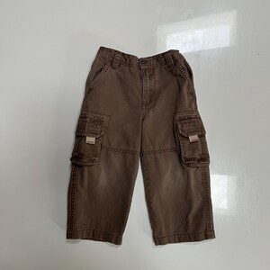May include: Brown cargo pants with two front pockets and two side pockets. The pants have a button and zipper closure and belt loops. The pants are made of a durable fabric and are suitable for casual wear.