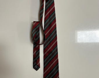 May include: A red, green, and black striped tie. The tie is made of a smooth fabric and features a classic design. The stripes are evenly spaced and run vertically down the length of the tie. The tie is displayed against a white background.