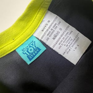 May include: A close-up of a black t-shirt with a neon green collar. A blue Disney-Pixar Toy Story tag is visible. The shirt's tag reads "BOYS 8" and includes fabric content and care instructions.