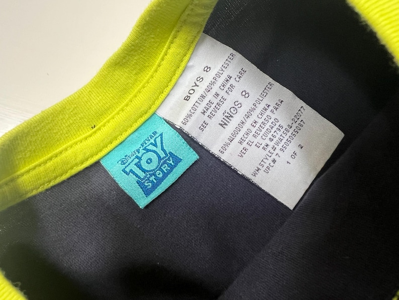 May include: A close-up of a black t-shirt with a neon green collar. A blue Disney-Pixar Toy Story tag is visible. The shirt's tag reads "BOYS 8" and includes fabric content and care instructions.