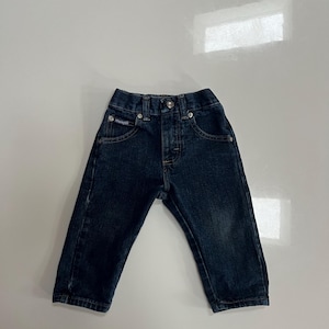 Op de afbeelding: Donkerblauwe spijkerbroek voor een peuter. De jeans heeft een knoop- en ritssluiting, voor- en achterzakken en het Wrangler-logo op de voorzak. De jeans is gemaakt van duurzaam denim materiaal.