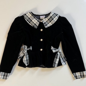 May include: A black velvet jacket with a plaid collar, cuffs, and bow accents. The jacket features a round collar, pearl-like buttons, and bows at the waist. The sleeves are long and the jacket has a fitted silhouette.