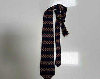 May include: A dark navy blue necktie featuring a repeating pattern of horizontal stripes. Each stripe contains a series of interconnected, chain-like links in a light tan or beige color, accented with thin, subtle red lines running through the center.