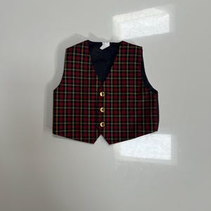 May include: A red, black, and yellow plaid vest with a black back and gold buttons. The vest has a V-neck and is likely for formal occasions or as part of a costume.