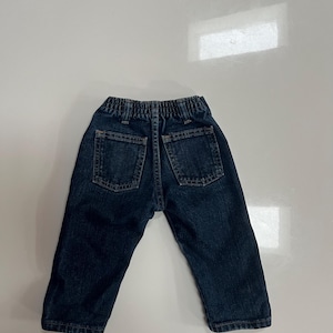 Op de afbeelding: Donkerblauwe spijkerbroek voor een peuter, met twee achterzakken en een elastische tailleband. De broek is ontworpen met een klassieke vijf-zakken-stijl en is gemaakt van duurzaam denim materiaal.