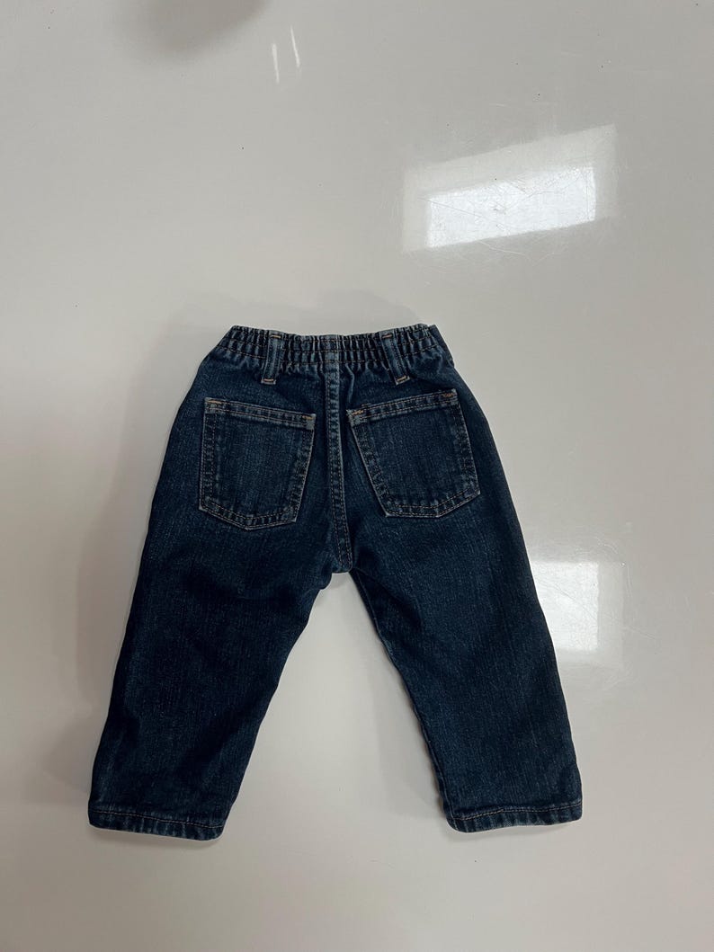 Op de afbeelding: Donkerblauwe spijkerbroek voor een peuter, met twee achterzakken en een elastische tailleband. De broek is ontworpen met een klassieke vijf-zakken-stijl en is gemaakt van duurzaam denim materiaal.
