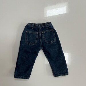 Op de afbeelding: Donkerblauwe spijkerbroek voor een peuter, met twee achterzakken en een elastische tailleband. De jeans is gemaakt van een stevig denim materiaal en heeft een klassieke, casual stijl.