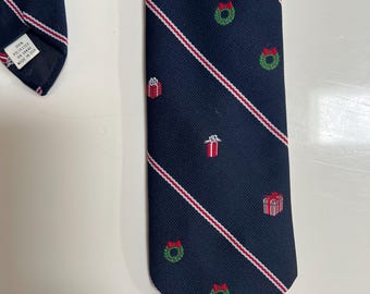 May include: Navy blue tie with diagonal red and white stripes. The tie features small green wreaths with red bows and red gift boxes. The tie is made of 100% polyester.