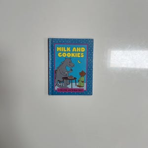 May include: A children's book titled "Milk and Cookies" with a blue cover featuring a cartoon illustration of a bear and a horse. The book has a yellow border and the text "A Frank Asch Bear Story".