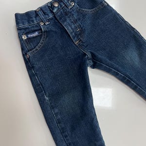Op de afbeelding: Donkerblauwe Wrangler-jeans van denim voor een peuter. De jeans hebben een knoop- en ritssluiting, voor- en achterzakken en het Wrangler-logo op de voorzak. Gemaakt van duurzaam denim materiaal.