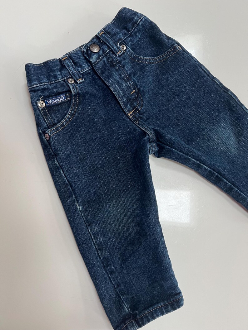 Op de afbeelding: Donkerblauwe Wrangler-jeans van denim voor een peuter. De jeans hebben een knoop- en ritssluiting, voor- en achterzakken en het Wrangler-logo op de voorzak. Gemaakt van duurzaam denim materiaal.