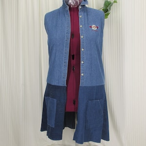May include: A sleeveless denim vest with a button-up front and two front pockets. The vest features a Hard Rock Cafe logo on the chest and is made of different shades of blue denim.