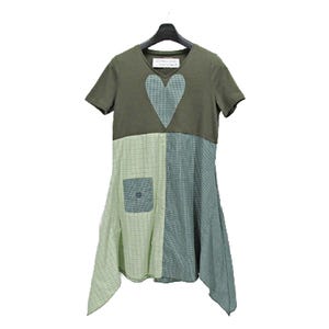May include: A short-sleeve dress featuring an olive green bodice with a central heart-shaped patch. The lower section is constructed from two contrasting panels of light green and dark green checkered fabric, including a small square pocket.