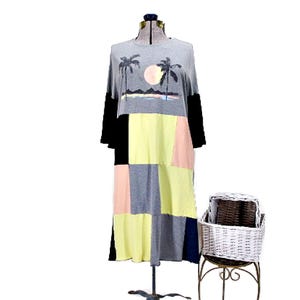May include: A knee-length dress featuring a grey top section with a graphic of palm trees and a sun over mountains. The lower portion consists of a color-blocked patchwork design in yellow, grey, peach, and black. It has long black sleeves.