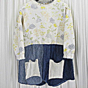 May include: A two-piece outfit featuring a white long-sleeved top with a floral pattern in yellow, green, and blue. The top is paired with a dark blue denim skirt with two white pockets. The outfit is displayed against a white background.