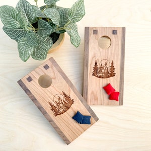 May include: Two wooden cornhole boards with a wolf howling at the moon design. The boards are made of cherry wood with walnut accents. The boards are set up for a game of cornhole, with red and blue bean bags on the boards.