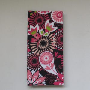 May include: A rectangular canvas with a floral paisley design. The pattern features pink, white, and green flowers on a black background. The canvas is a decorative item, possibly for wall art or home decor.