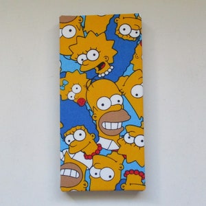 May include: A rectangular canvas featuring a repeating pattern of yellow cartoon characters on a blue background. The characters have yellow skin, large eyes, and various expressions. The canvas is mounted on a white wall.