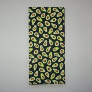 May include: A rectangular fabric item with a black background covered in a pattern of green and brown avocado halves. The avocados are in various orientations, creating a visually appealing design.