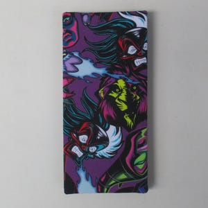 May include: A rectangular, purple fabric item featuring a repeating pattern of stylized, cartoonish faces in red, black, green, and yellow. Some faces have flames or blue accents. The item is likely a case or cover.
