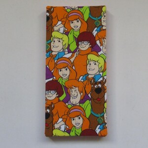 May include: Rectangular fabric featuring a colorful pattern of cartoon characters, including a brown dog, a redhead, and others. The design is a repeating pattern of the characters on a white background. The fabric is likely used for crafting or decorative purposes.