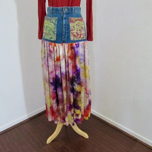 May include: A denim skirt with decorative pockets and a long, tie-dye skirt. The denim waistband has two pockets with patterned fabric. The skirt is a mix of colours, including purple, yellow, and pink.