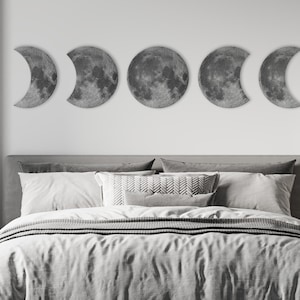 May include: Five gray crescent moon wall decor pieces arranged in a row above a gray headboard and white bedding.