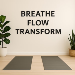 May include: Two grey yoga mats on a light wood floor in front of a white wall with the text "BREATHE FLOW TRANSFORM" in black letters.