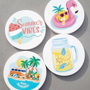 May include: Four round white coasters with summer themed designs. The first coaster features a watermelon popsicle with the text "Summer Vibes". The second coaster features a pineapple wearing sunglasses and a life vest floating on a pink flamingo. The third coaster features a mason jar filled with lemonade and lemon slices. The fourth coaster features a yellow and orange vintage van driving on a beach with palm trees and the text "Happy Summer".