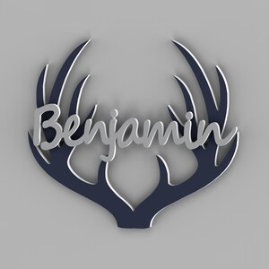 May include: A decorative wall art piece featuring the name "Benjamin" in silver script, set against a navy blue antler design with white accents. The artwork is displayed on a gray background.