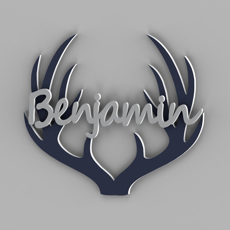 May include: A decorative wall art piece featuring the name "Benjamin" in silver script, set against a navy blue antler design with white accents. The artwork is displayed on a gray background.
