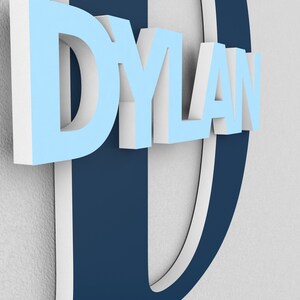 May include: A blue and white 3D name sign with the name "DYLAN" in white letters on a blue background. The letter "D" is a large, blue, 3D letter with a white outline.