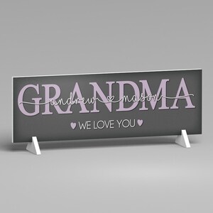 May include: A rectangular sign with the word "GRANDMA" in lavender letters. Below the word "GRANDMA" is the names "andrew mason" in a cursive font. The sign also includes the phrase "WE LOVE YOU" with heart symbols.