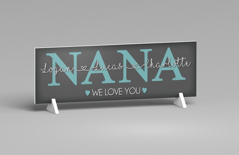 May include: A rectangular sign with the word "NANA" in teal block letters. Below the word "NANA" are the names "Logan", "Lucas", and "Charlotte" in a cursive font. The words "WE LOVE YOU" are below the names. The sign is gray and supported by two white stands.